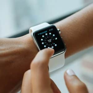 A close-up of a person wearing an Apple Watch with a white band. The screen displays weather information for Montreal, showing a temperature of 19 degrees. The person is interacting with the watch by touching the screen, showcasing how this device not only keeps you informed but could one day save your life.